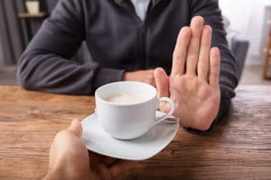 person putting hand up to refuse cup of coffee